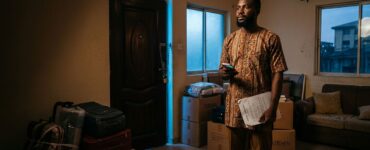 A Nigerian tenant holds tenancy papers inside a room with packed boxes and a locked door.