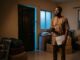 A Nigerian tenant holds tenancy papers inside a room with packed boxes and a locked door.