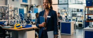 Nigerian student holding a logbook and laptop in a modern workplace.